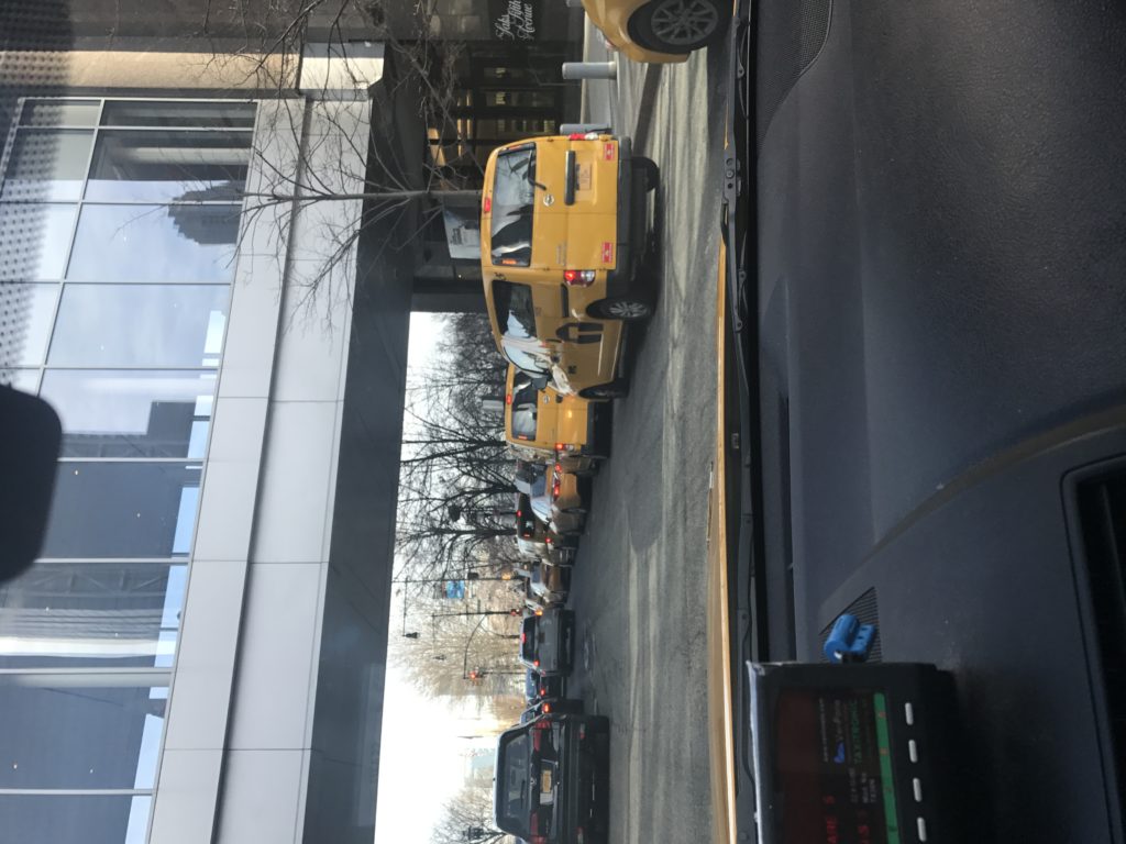 Yellow taxi parked at the curb seen from inside a car