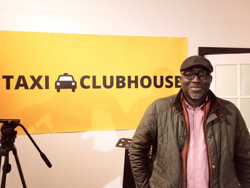 Man standing in front of the Taxi Clubhouse sign
