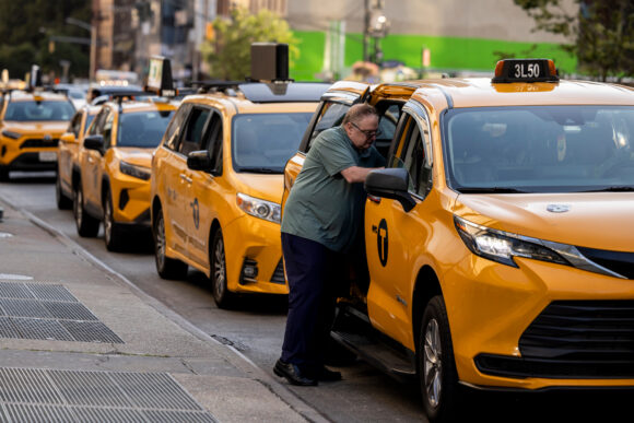 Driver standing at a yellow Toyota Sienna taxi in a row of cabs