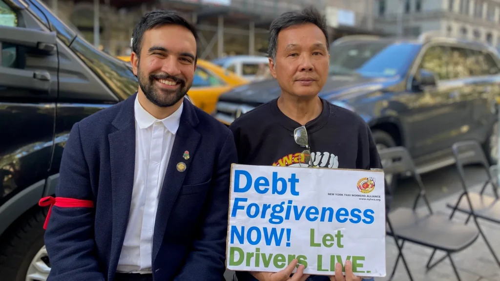 Zohran Mamdani with a taxi driver holding a Debt Forgiveness Now sign